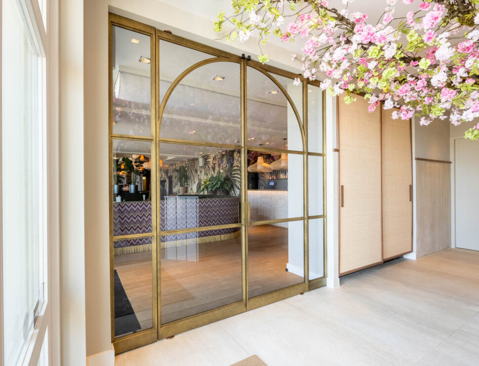 Luxe messing stalen schuifdeuren met glas en elegante boogdetails, als stijlvolle entree naar een chique interieur.